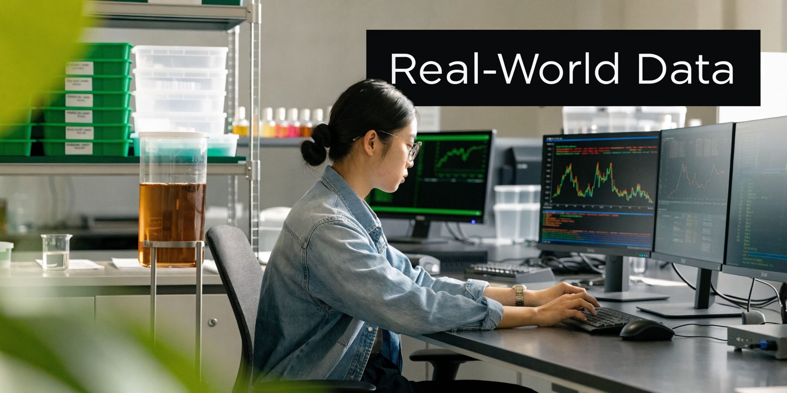 A woman working on computers with data visualizations and charts in a laboratory environment.
